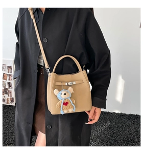 Detail view of khaki bucket bag featuring silver twist lock and cute bear charm accessory