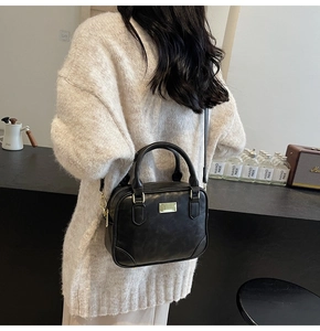 Detail of a vintage black leather crossbody bag styled with a white knit sweater