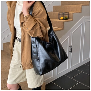 Detail of the black textured leather tote bag with metallic rivet ring and wide shoulder strap