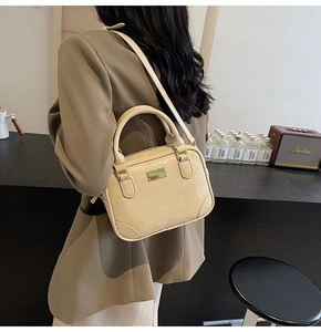 Macro detail of a beige vintage leather handbag featuring a golden metal logo plate and handles