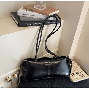 Detail of glossy black shoulder bag with drawstring folds and branded metal plaque