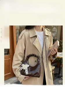 Détail d'un sac à main marron brillant avec poignée plissée et breloque noeud en perles