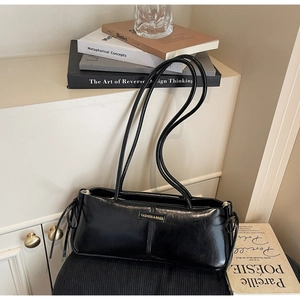 Detailed close-up of a black glossy shoulder bag featuring a golden fashion metal logo
