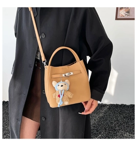 Detail of camel lychee leather bucket bag with metal twist lock and cute bear charm
