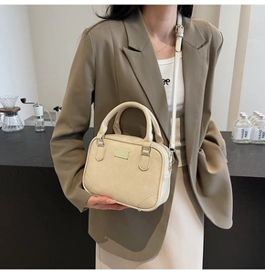 Detail of cream Boston handbag with matte PU texture and gold plaque on front