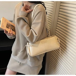 Detail of beige baguette bag showing side bow drawstring and textured PU leather