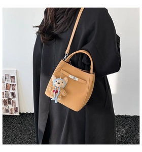 Detail of light brown bucket bag featuring a teddy bear charm and metal twist lock