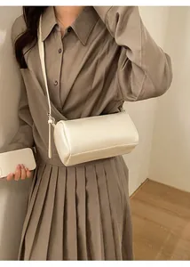 Minimalist cream white cylinder pillow bag with pebble leather texture worn on shoulder