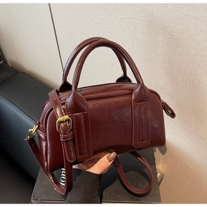 Détail du sac Boston bordeaux brillant avec poignées renforcées et garnitures métalliques dorées