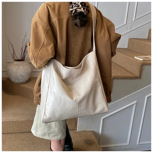 Minimalist beige tote bag in soft leather shown on shoulder with vintage textured background