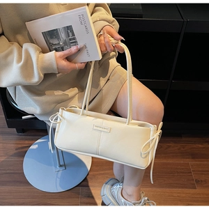 Detail of a creamy white baguette bag with bow accents and fashion label lettering