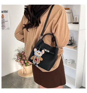 Detail of black pebbled leather bucket bag with silver lock and cute bear charm pendant