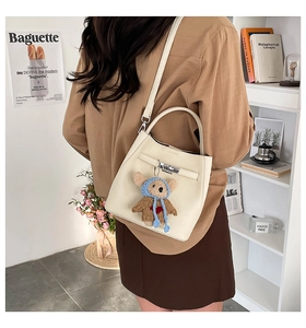 Detail of cream bucket bag with lychee grain leather, metal twist lock and bear charm