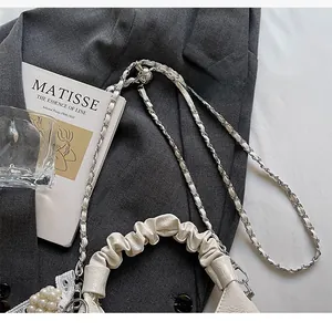 Détail du sac en cuir crème avec poignée plissée, chaîne en métal et breloque perle