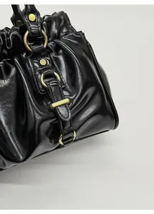 Close-up of black glossy pleated leather with vintage gold hardware on the handbag