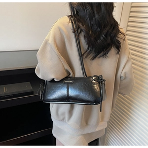 Close-up of black glossy baguette bag featuring vertical stitching and fashion metal plaque