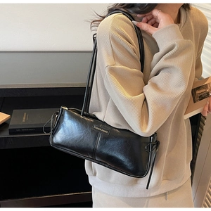 Detail of a black leather underarm bag with metal fashion tag and bow on a shoulder strap