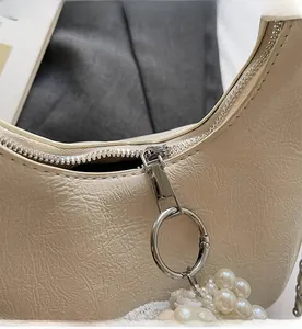 Détail du sac plissé beige avec fermeture éclair argentée et breloque en dentelle de perles