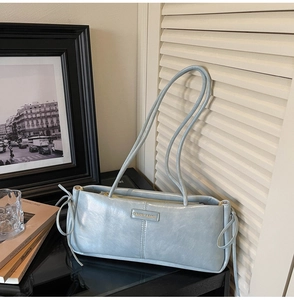 Detail of light blue-grey leather baguette bag with knotted decor and brand label