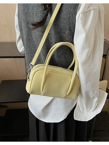 Detail of pale yellow crossbody bag featuring dual handles and silver hardware