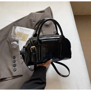 Détail d'un sac Boston en cuir verni noir avec quincaillerie dorée dans un cadre chic