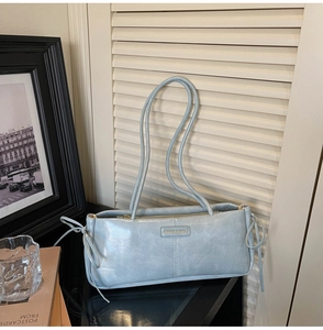 Detail of light blue faux leather baguette bag with side bow accents and metal zipper