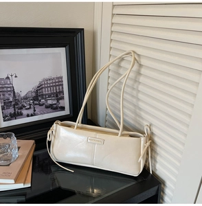 Detailed view of cream bow baguette bag with polished leather finish and fashion tag