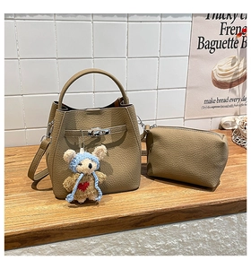Close-up of khaki pebbled leather bucket bag set with silver turn-lock and cute bear charm