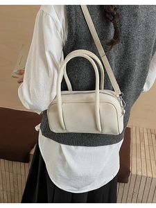Detail of cream rectangular bowling bag with double top handles and slim crossbody strap