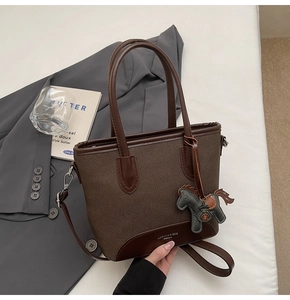 Detalle de bolso tote de cuero marrón oscuro con colgante de caballo sobre fondo blanco
