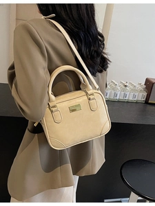 Minimalist beige crossbody handbag with double handles and golden plate on a model