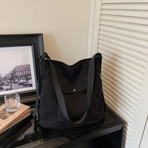 Detail of black corduroy tote bag featuring silver snap button pocket and wide shoulder strap