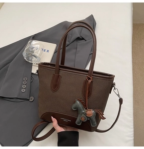 Detalle de un bolso cubo de lona marrón con ribetes de piel y colgante de caballo