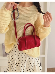Detail of red leather bowling bag with twin handles and crossbody strap on a model