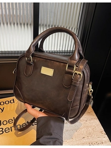 Retro dark brown crossbody handbag with dual handles and gold metal detail on stone background
