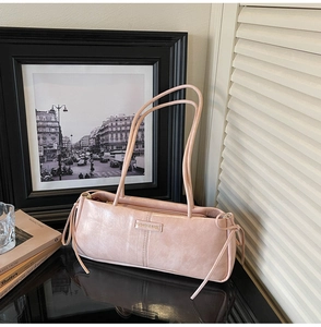 Detailed view of pink leather shoulder bag with golden metal logo and side drawstring knots