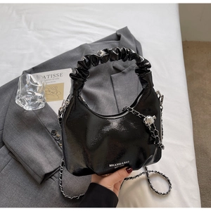 Détail du sac demi-lune en cuir verni noir avec poignée plissée et breloque ours