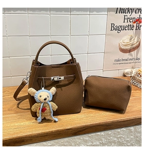 Close-up of brown pebbled leather bucket bag with silver lock and knitted bear charm