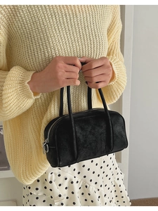 Detail of black bowling handbag with cracked texture worn by model in casual style