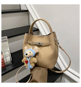 Detail of khaki pebbled leather bucket bag featuring a silver twist lock and bear charm