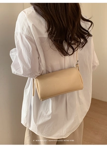 Rear view of a minimalist beige lychee pattern cylindrical crossbody bag on a model