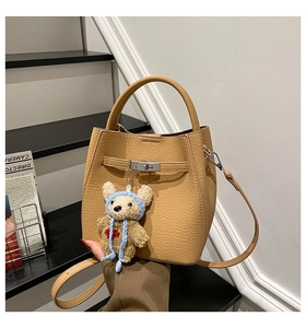 Detail of beige lychee grain leather bucket bag with metal lock and cute teddy bear charm