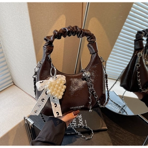 Détail du sac en cuir verni marron foncé avec pendentif cœur perlé et nœud en dentelle