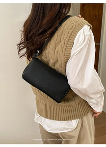 Detail of minimalist black pebbled leather cylinder bag showing texture and shoulder strap