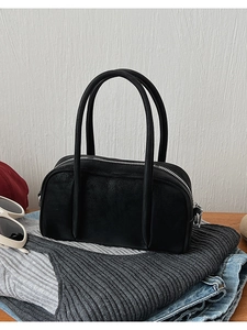 Close-up of black bowling handbag with silver zipper on a wooden table with sunglasses