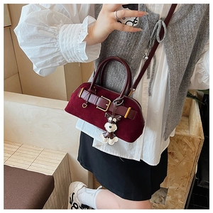 Macro shot of burgundy suede handbag with gold buckle and schnauzer charm detail