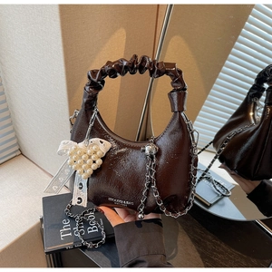 Détail d'un sac à main marron foncé brillant avec pendentif cœur perlé et nœud dentelle