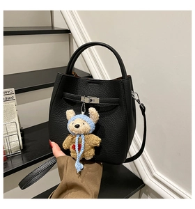 Detail of black lychee leather bucket bag with silver buckle and cute bear charm decoration