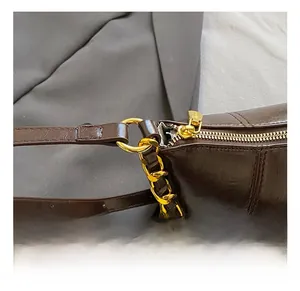 Detail of dark brown glossy leather bag with gold chain and premium metal zipper