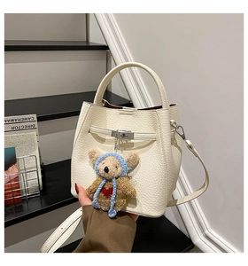 Close-up of white lychee leather bucket bag featuring a metal lock and cute bear charm